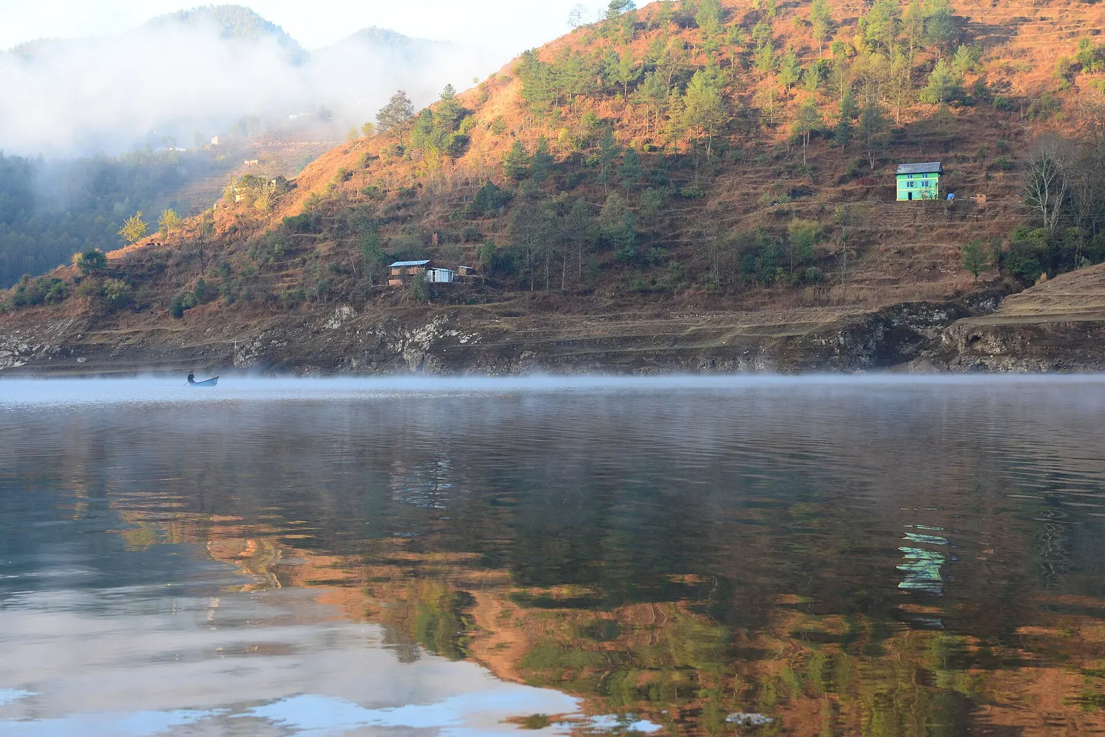 Calm water of the Kulekhani reservoir reflecting a sunlit hill.
