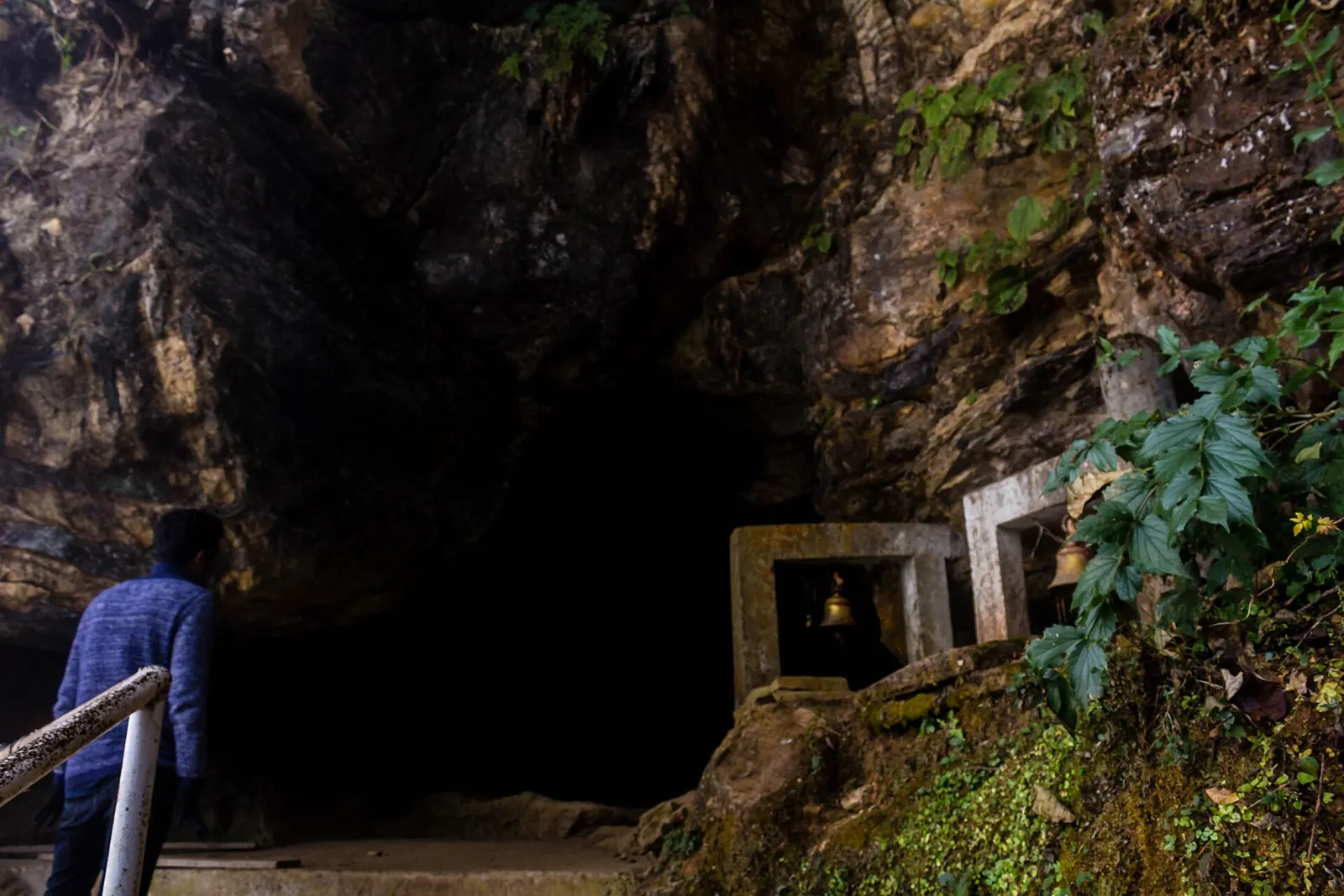 The entrance of Siddha Gufa, with small shrines set against the rock face and forest around it.