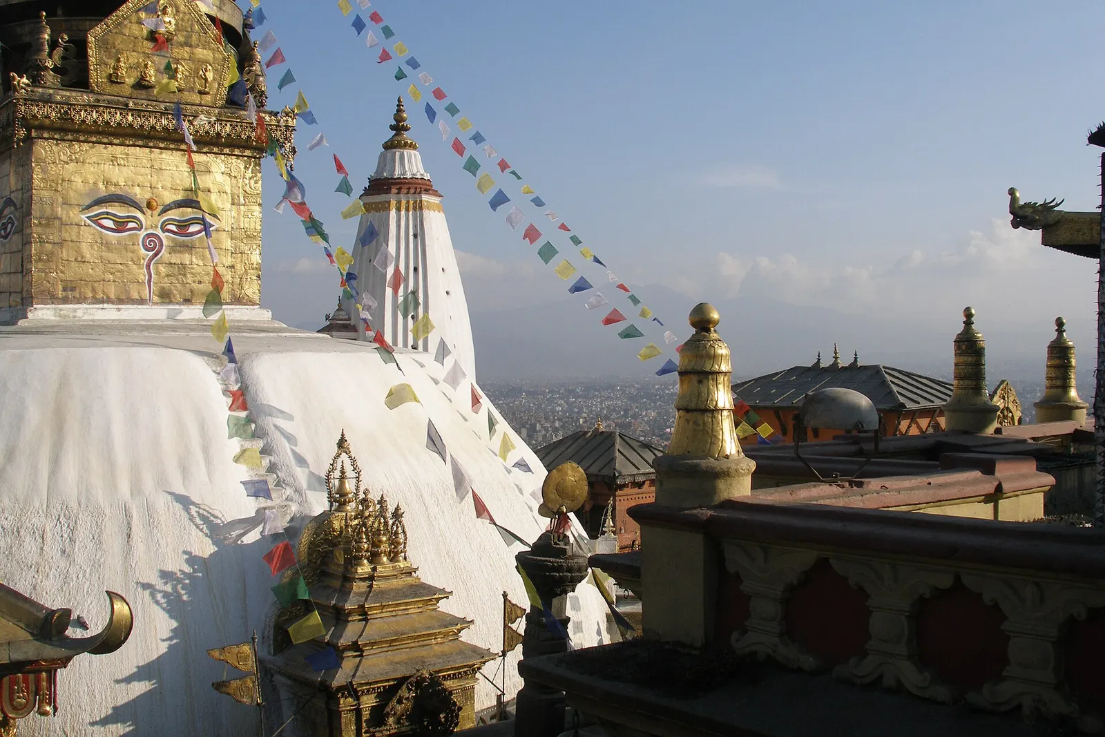 The white dome and gilded tower of Swayambhunath stupa with painted eyes, on its hilltop in Kathmandu.