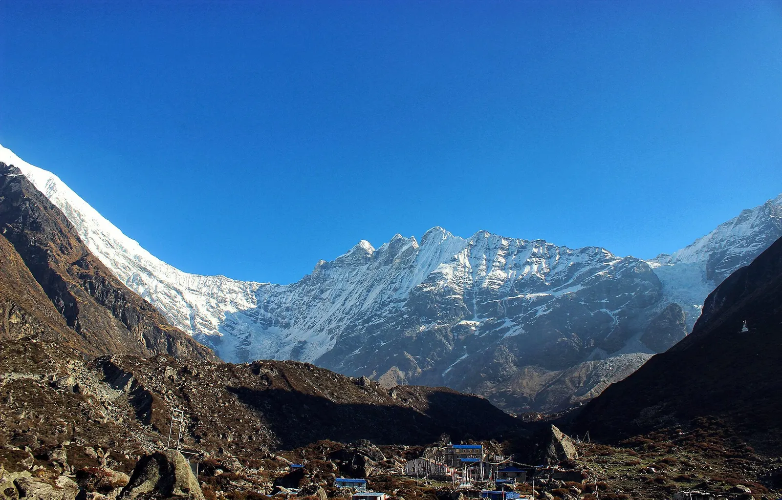 Snowy Langtang peaks rising above the Kyanjin valley under a deep blue sky, with village rooftops below