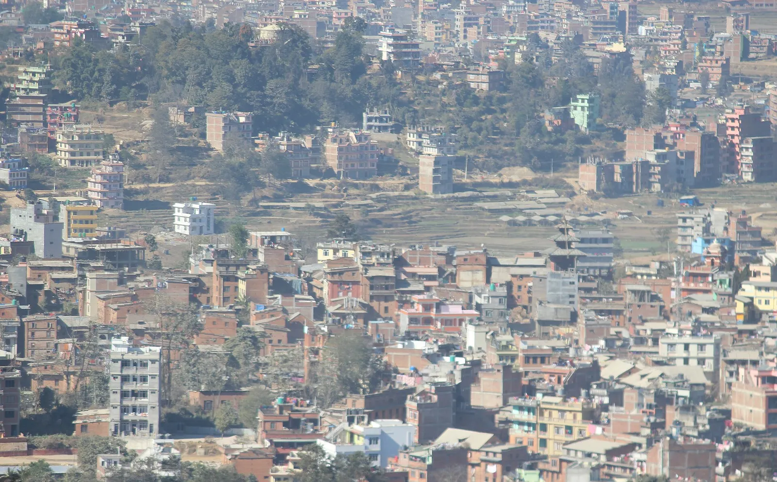 Houses of Dhulikhel spread across a ridge, seen from the hilltop Kali temple, with a temple roof in view.