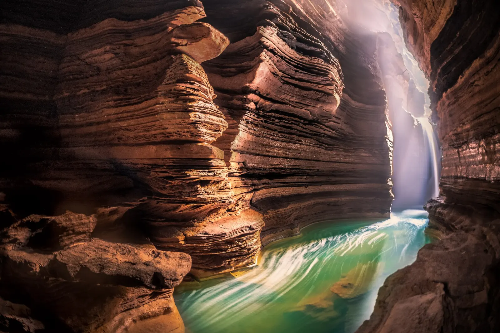 Layered rock walls inside Gupteshwor Cave, with light falling on the stream that flows on from Davis Falls.