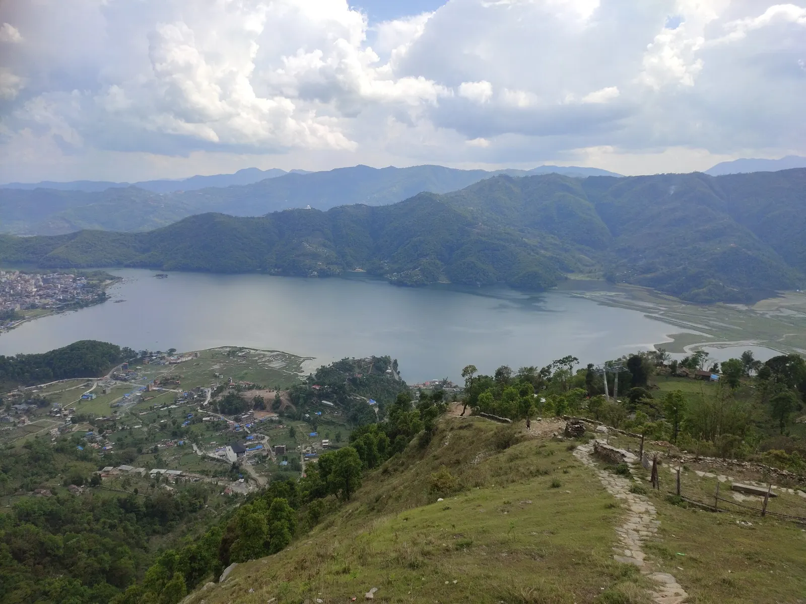 Phewa Lake stretching between green hills, seen from a grassy ridge trail above Pokhara.