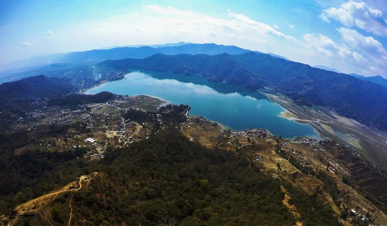 Phewa Lake curving below forested hills with Pokhara city spread across the valley floor.