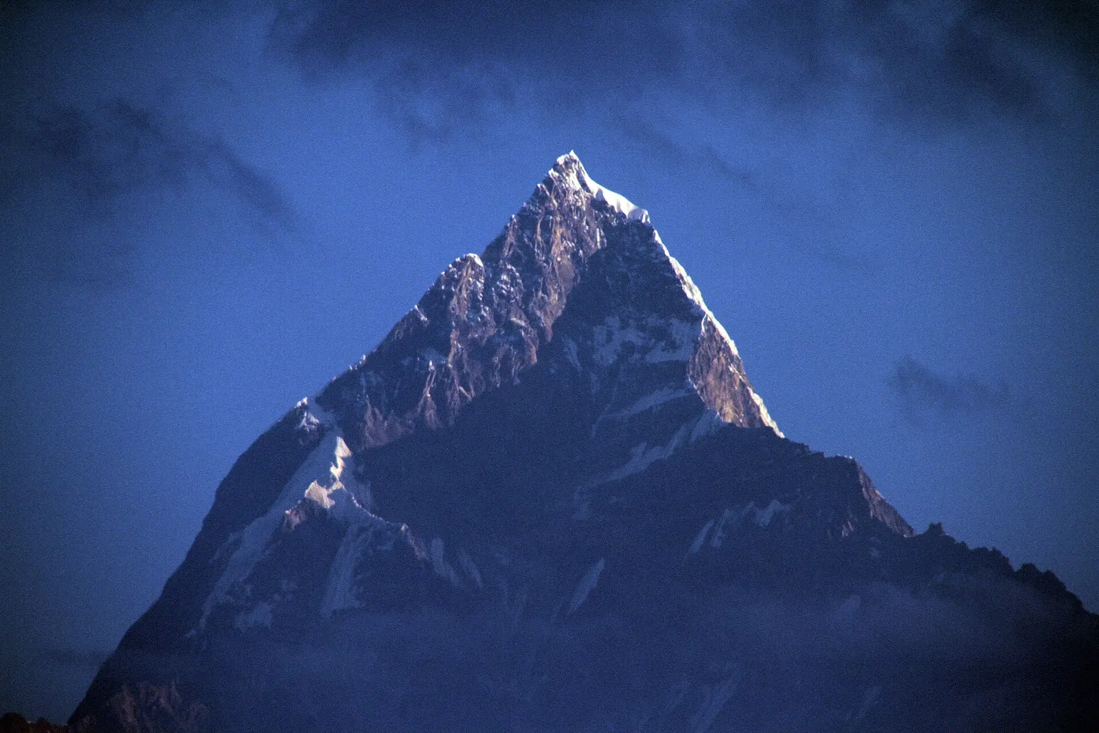 The pointed summit of Machhapuchhre against a deep blue pre-dawn sky, seen from Sarangkot.