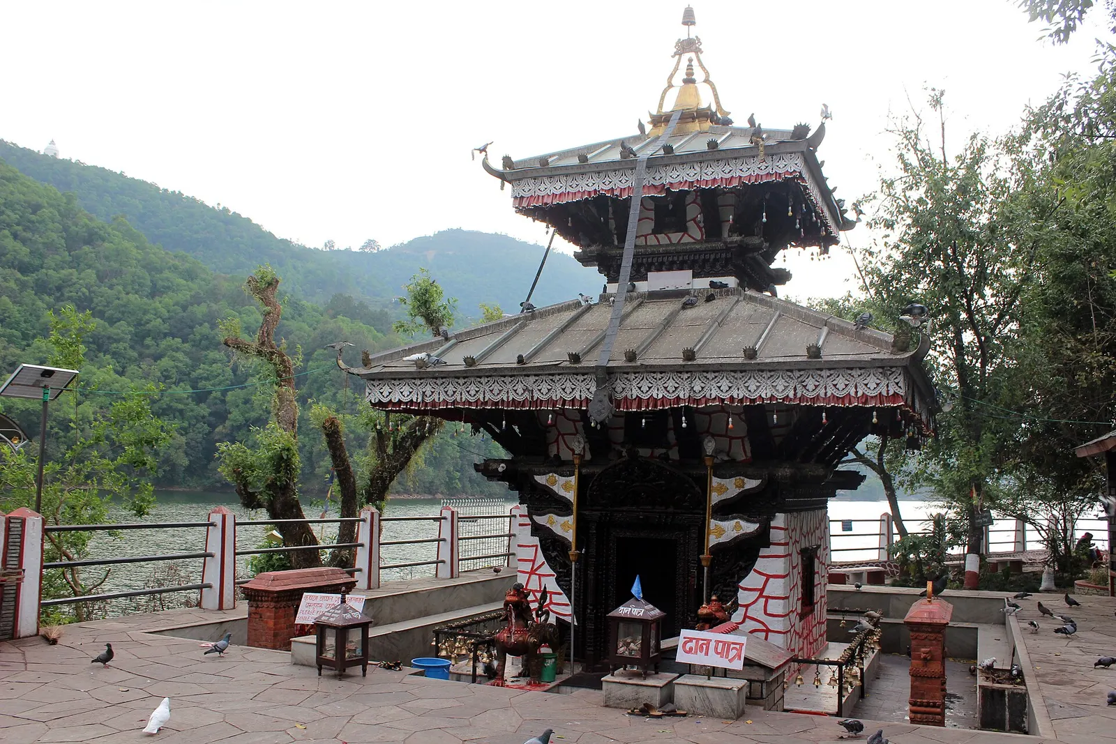 The two-tiered pagoda roof of the Tal Barahi temple with bells and a railing at the water's edge.
