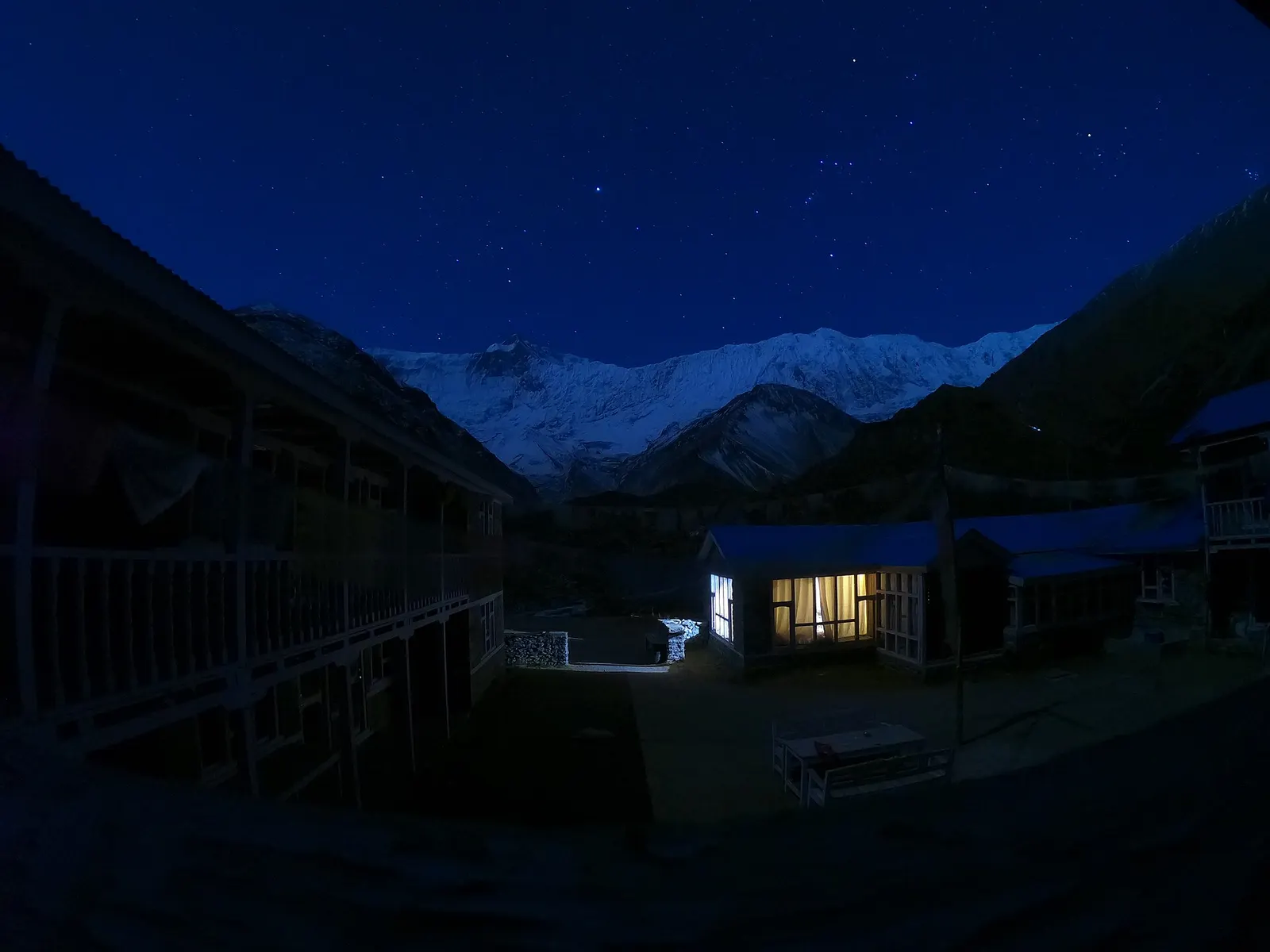 A lit lodge at Tilicho Base Camp at night, with moonlit snow peaks beyond.