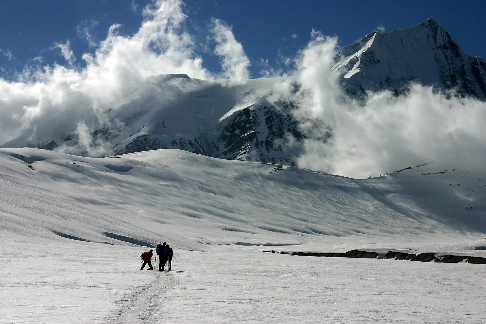 Two small figures crossing the snow-covered Hidden Valley beneath the peak of Sita Chuchura and drifting cloud.