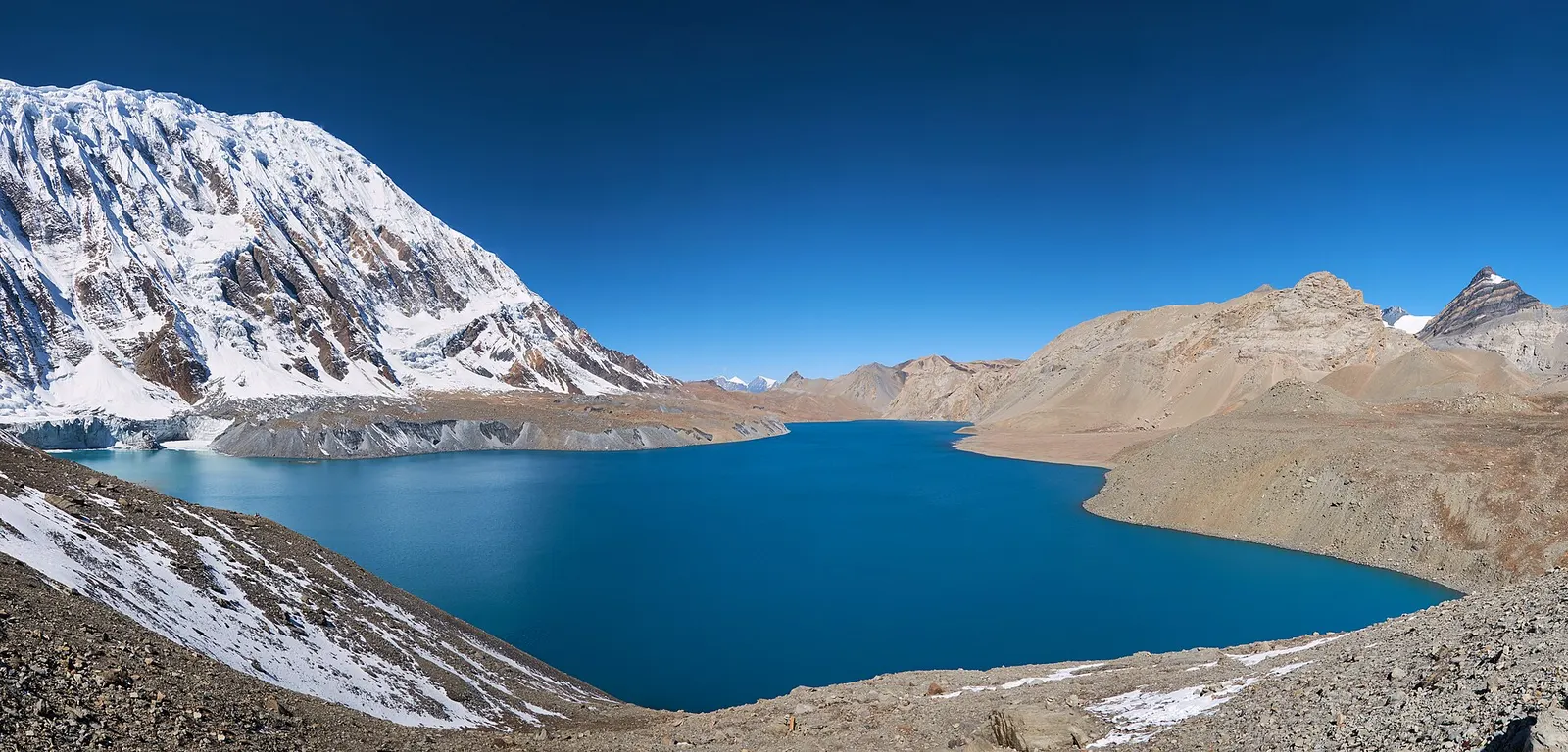 Deep-blue Tilicho Lake beneath the glaciated wall of Tilicho Peak and barren brown ridges